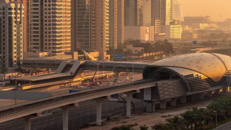 Foto de Edificio futurista de la estación de metro de Dubai y rascacielos de lujo detrás en Dubai Marina timelapse aérea por la mañana durante el amanecer. Tráfico en la carretera Sheikh Zayed, Emiratos Árabes Unidos - Imagen libre de derechos