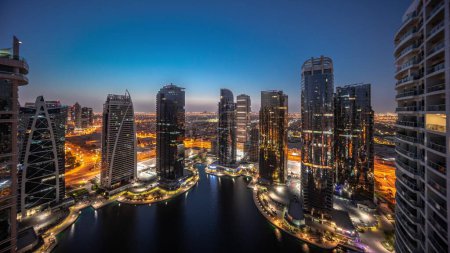 Téléchargez les photos : Panorama des grands bâtiments résidentiels du quartier JLT - passage aérien de nuit au jour - qui fait partie du quartier mixte du centre multi-commodités de Dubaï. Tours et gratte-ciel éclairés - en image libre de droit