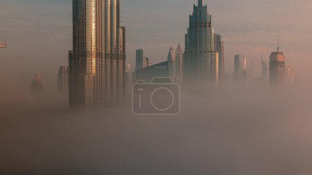 Foto de Aerial view of Dubai city early morning during fog . Sunrise at futuristic city skyline with skyscrapers and towers from above. Sun reflected from glass surface - Imagen libre de derechos