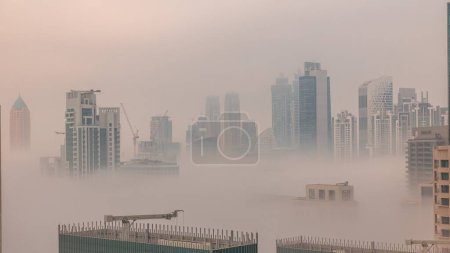 Foto de Dubai skyscrapers covered by morning fog in business bay district during sunrise . Aerial view from top of downtown in United Arab Emirates. - Imagen libre de derechos