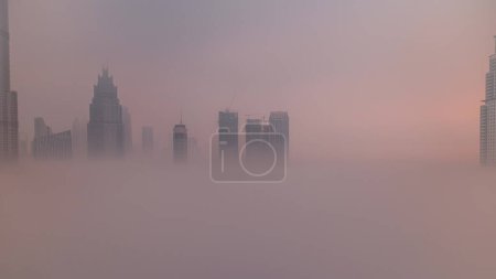 Téléchargez les photos : Aerial view morning fog covered Dubai International Financial Centre district . Office towers and hotels with modern skyscrapers and mall during sunrise - en image libre de droit