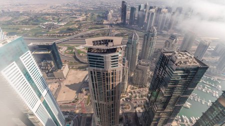 Photo for Fog covered skyscrapers in JLT district aerial . Top view from Dubai marina towers at evening time with golf course and traffic on highway - Royalty Free Image