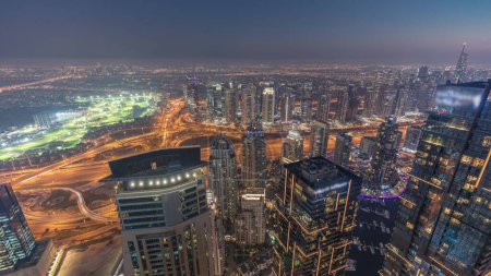 Téléchargez les photos : Panorama of Dubai Marina with JLT skyscrapers and golf course day to night transition , Dubai, United Arab Emirates. Aerial view from above towers after sunset - en image libre de droit