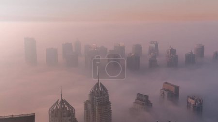 Téléchargez les photos : Fog covered JLT skyscrapers and marina towers near Sheikh Zayed Road aerial  during sunrise. Residential building hazy morning with warm colorful light - en image libre de droit