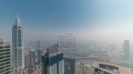 Photo for Towers covered by rare early morning winter fog above the Dubai Marina skyline with sun going up and skyscrapers rooftops aerial . Top view from above clouds. Dubai, UAE - Royalty Free Image
