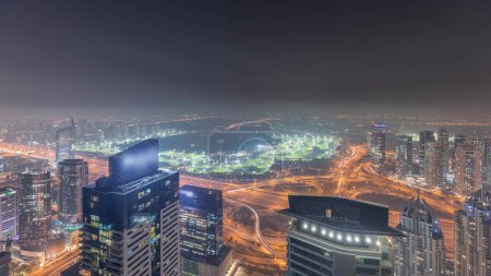 Téléchargez les photos : Panorama of Dubai Marina with JLT skyscrapers and golf course night , Dubai, United Arab Emirates. Aerial view from above towers. City lights illumination - en image libre de droit