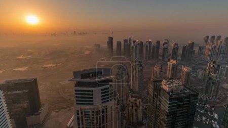 Téléchargez les photos : Panorama of Dubai Marina with JLT skyscrapers and golf course during sunrise , Dubai, United Arab Emirates. Aerial view from above towers foggy morning. City skyline with orange sky - en image libre de droit