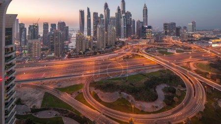 Téléchargez les photos : Panorama of Dubai Marina highway intersection spaghetti junction day to night transition . Illuminated tallest skyscrapers on a background. Aerial top view from JLT district after sunset - en image libre de droit