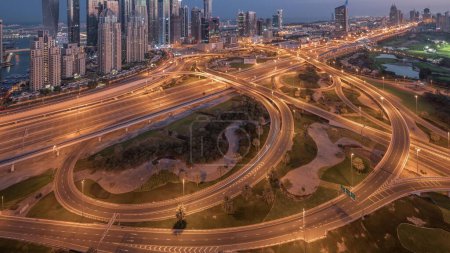 Photo for Panorama of Dubai Marina highway intersection spaghetti junction night to day transition . Illuminated tallest skyscrapers and golf course on a background. Aerial top view from JLT district before sunrise - Royalty Free Image