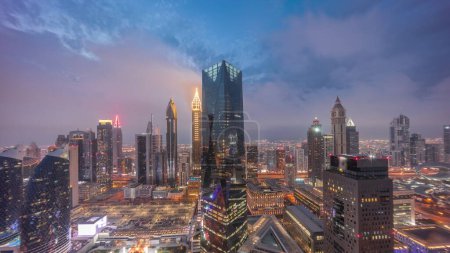 Téléchargez les photos : Panorama of futuristic skyscrapers after sunset in financial district business center in Dubai on Sheikh Zayed road day to night transition . Aerial view from above with cloudy sky - en image libre de droit