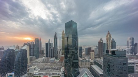 Foto de Panorama of futuristic skyscrapers with sunset in financial district business center in Dubai on Sheikh Zayed road . Aerial view from above with colorful cloudy sky - Imagen libre de derechos