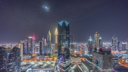 Téléchargez les photos : Panorama of futuristic skyscrapers in financial district business center in Dubai on Sheikh Zayed road during all night . Aerial view from above with illuminated towers and moon - en image libre de droit