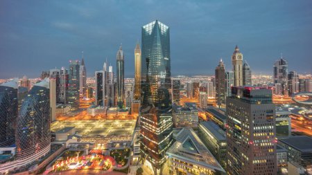 Téléchargez les photos : Panorama of futuristic skyscrapers in financial district business center in Dubai on Sheikh Zayed road night to day transition . Aerial view from above with illuminated towers with sunrise and long shadows - en image libre de droit