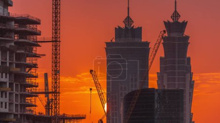 Téléchargez les photos : Close up view to Dubai's business bay towers at sunset aerial . Rooftop view of some skyscrapers and new towers under construction. Orange sky with buildings silhouette - en image libre de droit