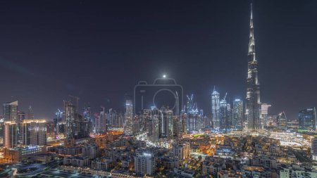 Foto de Dubai Downtown during all night with moon and lights turning off  with tallest skyscraper and other illuminated towers panoramic view from the top in Dubai, United Arab Emirates. - Imagen libre de derechos