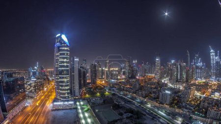 Téléchargez les photos : Panorama of Dubai's business bay and downtown towers during all night aerial . Rooftop view of some skyscrapers and new towers under construction and moon on the sky - en image libre de droit