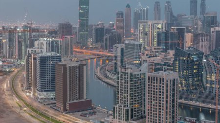 Téléchargez les photos : Skyline with modern architecture of Dubai business bay illuminated towers night to day transition . Aerial view with canal and construction site before sunrise - en image libre de droit