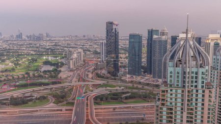 Téléchargez les photos : Huge highway crossroad junction between JLT district and Dubai Marina intersected by Sheikh Zayed Road aerial day to night transition  after sunset. Golf course near towers and skyscrapers with busy traffic - en image libre de droit