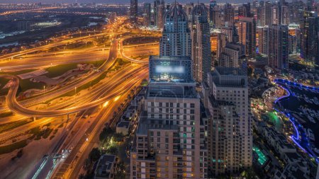 Foto de Dubai marina and JLT illuminated skyscrapers along Sheikh Zayed Road with traffic on big junction aerial night to day transition  before sunrise. Residential and office buildings from above. - Imagen libre de derechos