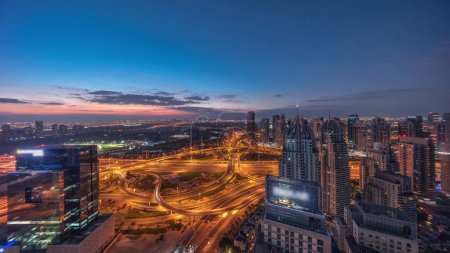Téléchargez les photos : Huge highway crossroad junction between JLT district and Dubai Marina intersected by Sheikh Zayed Road aerial night to day transition panoramic . Golf course near illuminated towers and skyscrapers with busy traffic - en image libre de droit