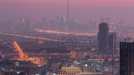 Photo for Dubai Downtown with financial district skyline row of skyscrapers with tallset tower aerial night to day transition . Overview in a far distance from Dubai marina rooftop. Villa houses before sunrise. UAE - Royalty Free Image