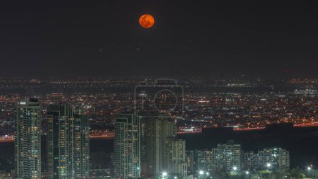 Foto de Moon rising over greens and al barsha heights district area night  from Dubai marina. Towers and skyscrapers with traffic on roads from above - Imagen libre de derechos
