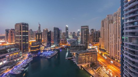 Foto de Aerial panoramic view to Dubai marina illuminated skyscrapers around canal with floating yachts night to day transition . White boats are parked in yacht club before sunrise - Imagen libre de derechos