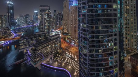 Photo for Panorama showing aerial view to Dubai marina illuminated skyscrapers around canal with floating yachts night . Towers in jlt and jbr districts. White boats are parked in yacht club - Royalty Free Image