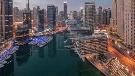 Téléchargez les photos : Aerial view to Dubai marina and jbr illuminated skyscrapers around canal with floating yachts night to day transition . White boats are parked in yacht club before sunrise - en image libre de droit