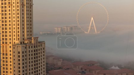 Téléchargez les photos : Bluewaters island with modern architecture and ferris wheel covered by morning fog aerial . New leisure and residential area near Dubai marina and JBR beach after sunrise - en image libre de droit