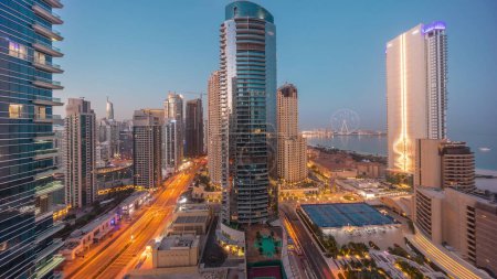 Téléchargez les photos : Panoramic view of the Dubai Marina and JBR area and the famous Ferris Wheel aerial night to day transition  and illuminated skyscrapers before sunrise - en image libre de droit