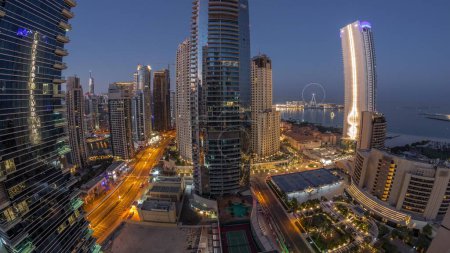 Photo for Panorama of the Dubai Marina and JBR area and the famous Ferris Wheel aerial night to day transition . Illuminated skyscrapers during sunrise with long shadows - Royalty Free Image