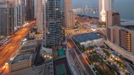 Téléchargez les photos : Panoramic view of the Dubai Marina and JBR area and the famous Ferris Wheel aerial night to day transition . Illuminated skyscrapers during sunrise with long shadows - en image libre de droit