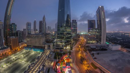 Foto de Panorama of Dubai International Financial district night to day transition . Aerial view of business office towers during sunrise. Illuminated skyscrapers with hotels and shopping malls near downtown - Imagen libre de derechos