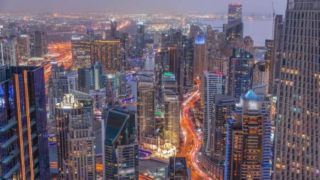 Foto de Skyline panoramic view of Dubai Marina and JBR showing canal surrounded by illuminated skyscrapers along shoreline aerial day to night transition . Traffic on curved road after sunset. DUBAI, UAE - Imagen libre de derechos