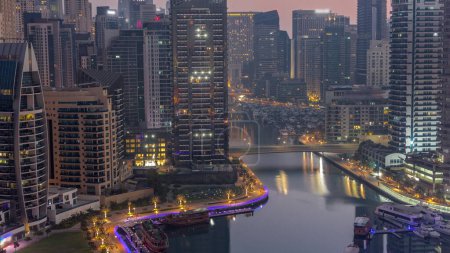 Photo for Dubai Marina with boats and yachts parked in harbor and illuminated skyscrapers around canal aerial night to day transition  before sunrise. Towers along waterfront - Royalty Free Image