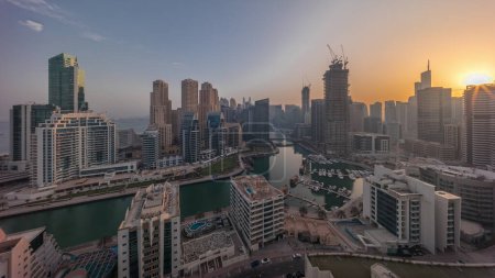 Foto de Dubai Marina with boats and yachts parked in harbor and skyscrapers around canal aerial  during all day from sunrise. Shadows moving fast. Towers of JBR district on a background - Imagen libre de derechos