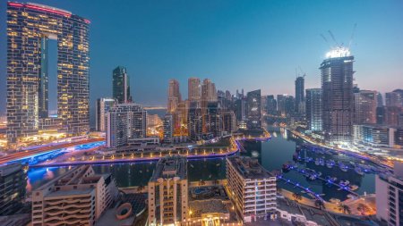 Foto de Dubai Marina panorama with boats and yachts parked in harbor and illuminated skyscrapers around canal aerial night to day transition  before sunrise. Towers of JBR district on a background - Imagen libre de derechos