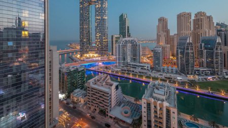 Photo for Dubai Marina skyscrapers and JBR district before sunrise with illuminated luxury buildings and resorts aerial night to day transition . Waterfront with palms and boats floating in canal - Royalty Free Image
