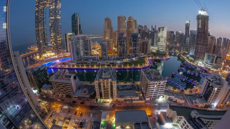 Téléchargez les photos : Panorama of Dubai Marina with boats and yachts parked in harbor and illuminated skyscrapers around canal aerial night to day transition  before sunrise. Towers of JBR district on a background - en image libre de droit