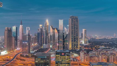 Foto de Panorama of Dubai Financial Center district with tall skyscrapers with illumination day to night transition . Aerial view to towers along busy highway after sunset - Imagen libre de derechos