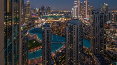 Foto de Aerial view of a big futuristic city with lake and fountains day to night transition . Business bay and Downtown district with many skyscrapers and traditional houses, Dubai, United Arab Emirates skyline. - Imagen libre de derechos