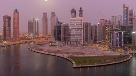 Téléchargez les photos : Cityscape of skyscrapers in Dubai Business Bay with peninsula on water canal aerial night to day transition  with Moon setting down. Modern skyline with illuminated towers and waterfront before sunrise - en image libre de droit