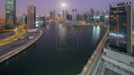 Photo for Cityscape of skyscrapers in Dubai Business Bay with water canal aerial night to day transition  with Moon setting down. Modern skyline with illuminated towers and waterfront before sunrise - Royalty Free Image