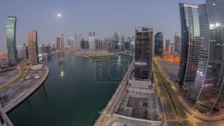 Téléchargez les photos : Cityscape panorama of skyscrapers in Dubai Business Bay with water canal aerial night to day transition  with Moon setting down. Modern skyline with illuminated towers and waterfront before sunrise - en image libre de droit