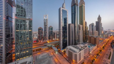 Foto de Aerial panorama of Dubai International Financial District with many skyscrapers night to day transition . Traffic on a road near multi storey parking with rooftop swimming pool. Dubai, UAE. - Imagen libre de derechos
