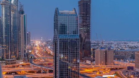 Téléchargez les photos : Dubai city skyline panoramic view with metro and cars moving on city's busiest highway aerial night to day transition . Junction surrounded by skyscrapers before sunrise - en image libre de droit