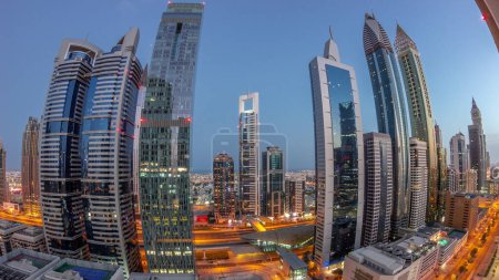 Foto de Panorama of Dubai International Financial District with many skyscrapers night to day transition aerial  during sunrise. Traffic on a road near metro station. Dubai, UAE. - Imagen libre de derechos