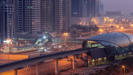 Téléchargez les photos : Futuristic building of Dubai metro station and luxury skyscrapers behind in Dubai Marina aerial night to day transition  before sunrise. Traffic on Sheikh Zayed road highway, United Arab Emirates - en image libre de droit