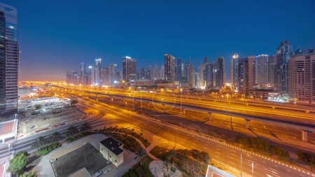 Téléchargez les photos : Dubai Marina skyscrapers and Sheikh Zayed road with metro railway aerial night to day transition panoramic . Traffic on a highway near modern towers before sunrise, United Arab Emirates - en image libre de droit